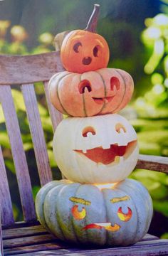 three pumpkins stacked on top of each other with faces painted on them, sitting on a wooden chair