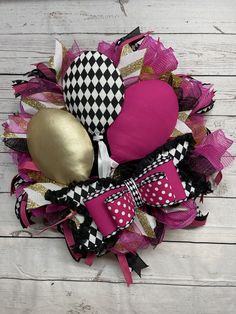 a wreath with pink, black and gold items on it sitting on a white wooden surface