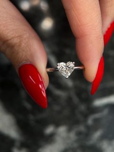 a woman's hand with red nail polish holding a diamond ring