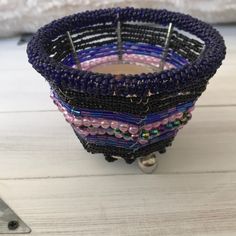 a purple and black beaded candle holder on a white wooden table next to a pair of scissors