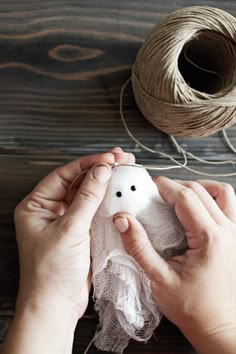 two hands are working on something that looks like a bird ornament, with yarn and twine in the background