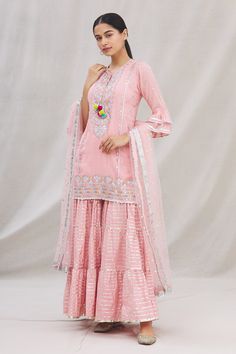 Pink kurta with all-over floral embroidery, notched round neckline and frilled hem sleeves. Comes with sharara and net dupatta.
Component: 3
Embroidered
Neckline: Round
Sleeve Length: Three Quarter
Fabric: Kurta: Cotton Silk; Sharara: Cotton; Dupatta: Net
Color: Pink
Notched round neckline
Tie-up with tassels
Frilled hem sleeves
Embroidered sharara
Elasticated waist
Frill detailing at the hem
Embellished dupatta with lace trim - Aza Fashions Navratri Sharara With Straight Kurta And Floral Embroidery, Diwali Sharara With Floral Embroidery And Straight Kurta, Diwali Floral Embroidery Sharara With Straight Kurta, Wedding Sharara With Straight Kurta And Floral Embroidery, Wedding Sharara With Floral Embroidery And Straight Kurta, Traditional Drape Sharara With Floral Embroidery For Eid, Designer Chanderi Sharara With Floral Embroidery, Designer Anarkali Sharara With Floral Embroidery, Floral Embroidered Sharara For Designer Wear And Diwali