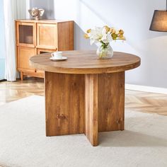 a wooden table sitting on top of a white rug next to a vase filled with flowers