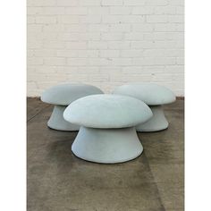 two white stools sitting next to each other on concrete flooring in front of a brick wall