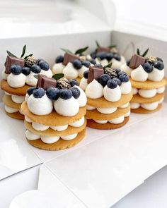 small desserts with blueberries and cream on them are displayed in a white box