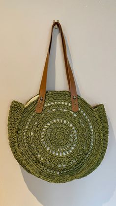 a green bag hanging on the wall next to a brown leather handle and tan straps