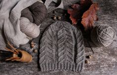 a knitted hat sits next to some yarn and autumn leaves on a wooden surface