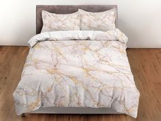 a bed with white and gold marbled sheets on top of wooden flooring next to a gray velvet headboard