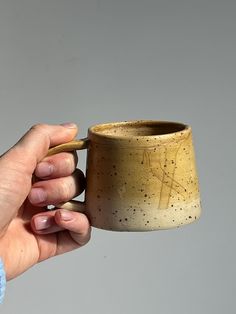 a hand holding a ceramic cup with speckled paint