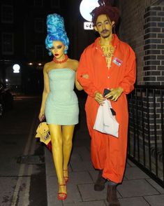 a man and woman in costumes walking down the street at night with neon colored hair