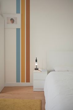 a white bed sitting in a bedroom next to a wall painted with multicolor stripes