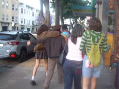 three people walking down the sidewalk in front of parked cars