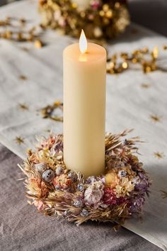 a lit candle sitting on top of a table covered in dried flowers and leaves with gold confetti around it