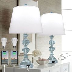 two lamps sitting on top of a dresser next to a phone and other items in front of a mirror