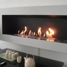 a modern fireplace with lit flames in the center and vases next to it on a table