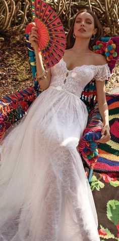 a woman in a white dress sitting on a colorful rug holding an umbrella and posing for the camera