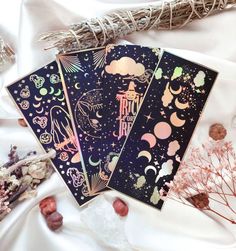 three cards with designs on them sitting next to dried flowers