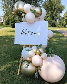 a sign that is sitting in the grass with balloons and greenery on top of it