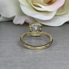 a white rose sitting next to a gold ring on top of a gray tablecloth