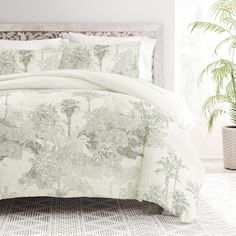 a bed with white and green comforters in a room next to a plant on the floor