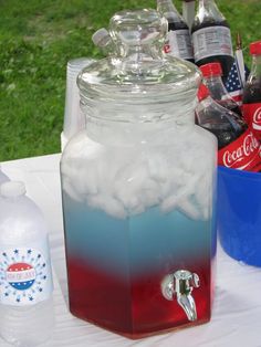 there is a cooler with ice and soda in it on the table outside near other drinks