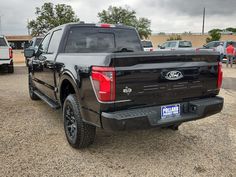 the back end of a black truck parked in a lot with other trucks and people