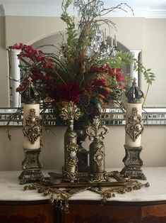 three candles are sitting on a table with flowers in the mirror behind them and an ornate candle holder