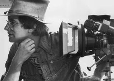 black and white photograph of a man with a hat on holding a camera in front of him