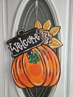 a welcome sign hanging on the front door of a house with pumpkins painted on it