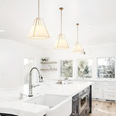 a large white kitchen with two sinks and three lights hanging from the ceiling above it