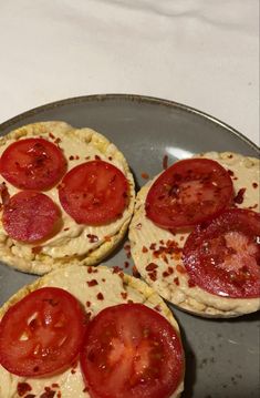 three small pizzas with tomatoes on them sitting on a metal plate, ready to be eaten