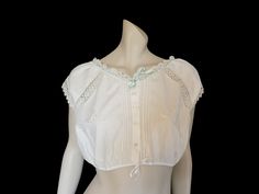 Antique corset cover reinvented as a beautiful cropped summer blouse. The blouse has tiny sleeves of cotton bobbin lace, as well as inserted lace panels and lace trim at the neck. Hand embroidery and eyelet work are featured front and back. Pin tucks at centre front and back. Closes at the front with shell buttons. The blue ribbon has been added to the neck, you can easily remove it if you prefer. I have altered the waistband - I removed the original band which was made to fit a tiny corseted waist, and replaced it with a binding of cotton tape, threaded through with narrow satin ribbon to tie at bottom front. Fabric and lace are all cotton. Beautifully handmade item - 1900s-1910s. Size - Medium  Best fit bust 92-94 cm (36-37") Under bust 76 cm (30") Shoulders 44 cm (17.5") Length 37.5 cm Fitted Lace Patchwork Crop Top, Fitted Crop Top With Lace Patchwork, Fitted Cropped Top With Lace Collar, Fitted Cropped Crop Top With Lace Patchwork, Lace Patchwork Crop Top For Summer, Spring Cotton Tops With Contrast Lace, Cotton Top With Contrast Lace For Summer, Cropped Tops With Lace Collar For Summer, Summer Cropped Tops With Lace Collar