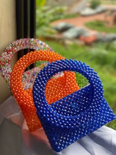 three different colored bags sitting on top of a window sill