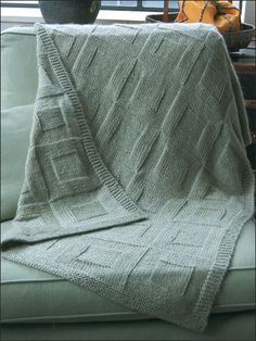 a green couch with a knitted blanket on it's back next to a potted plant