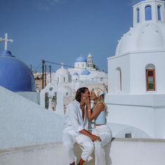 a man and woman are kissing in front of a white building with blue domes on the roof