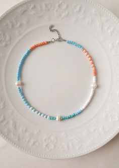 a white plate with a blue and orange beaded necklace on it's side