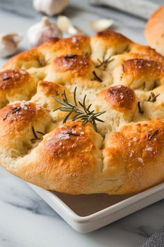 a close up of a bread dish on a plate with garlic and rosemary sprigs