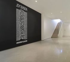 an empty room with stairs leading up to the second floor and a large sign on the wall that says joy division