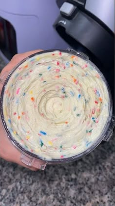 a person holding a cake in front of a crockpot with sprinkles on it