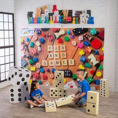 two children playing with wooden blocks and dices in front of a large board game