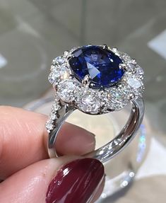 a close up of a person's hand holding a ring with a blue and white diamond