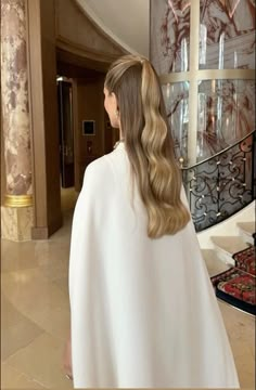 a woman with long blonde hair wearing a white cape and standing in front of a staircase