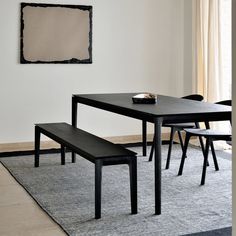 a black table and bench in a white room with a large painting on the wall