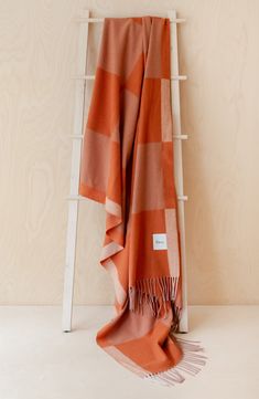 an orange and white blanket sitting on top of a wooden shelf next to a ladder