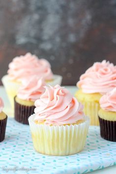 cupcakes with pink frosting sitting on a blue and white napkin next to each other