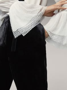 a woman in white blouse and black pants holding her hand over her shoulder with lace on it