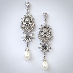 A classy pair of bridal earrings in art deco vintage inspired style. The flawlessly faceted cubic zirconia stones capture the light in a dazzling array of sparkles, while the delicate white pearls add fluidity and motion. The earrings are rhodium / rose gold / yellow gold plated for a bright finish which enhances the intricate detailing and conveys a modern take on old elegance. Length 2.5" (approx. 6.3cm); Width: 0.6" (approx. 1.5cm); Weight: 4.9g Available in Silver, Rose Gold and Yellow Gold Classic Diamond White Chandelier Earrings, Classic Diamond White Chandelier Earrings With Diamond Accents, Classic Bridal Earrings With Elegant Design For Evening, Classic Elegant Bridal Earrings For Evening, Classic Elegant Design Bridal Earrings For Evening, Classic Cubic Zirconia Chandelier Earrings For Formal Occasions, Classic Formal Chandelier Earrings In Cubic Zirconia, Classic Cubic Zirconia Earrings With Elegant Design, Glamorous Wedding Diamond Earrings With Accents