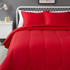 a bed with red sheets and pillows on top of it in a gray room next to a white night stand