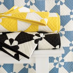 three folded quilts sitting on top of a white bench in front of a blue and yellow wall