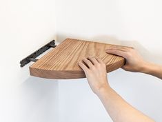 a person holding onto a wooden shelf with black brackets on the wall behind it,